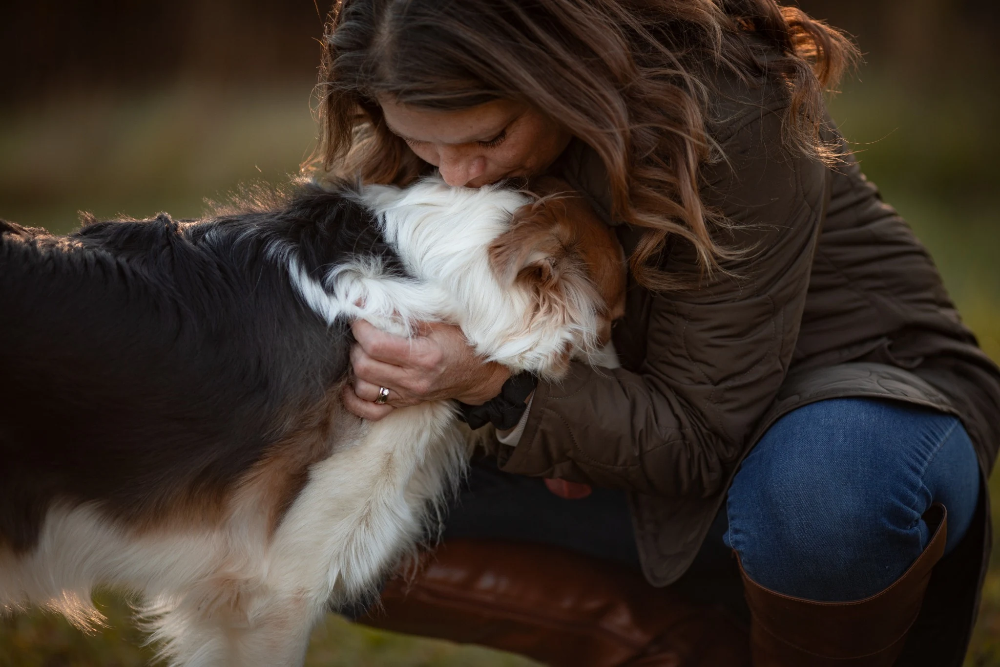 A woman embracing and kissing a Border Collie outdoors